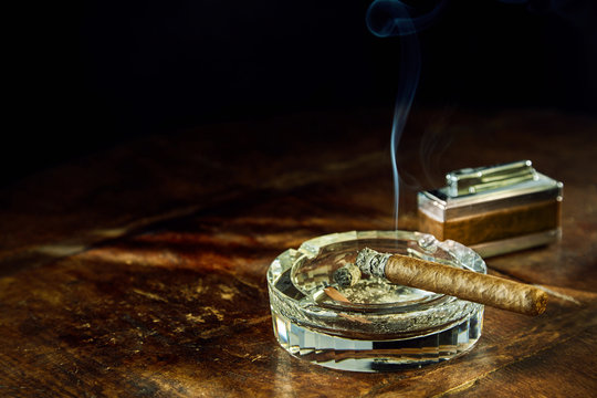 Smoking cigar sitting in glass ashtray on table