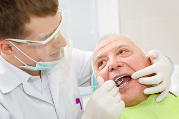 Closeup portrait of young dentist  treating senior elderly man