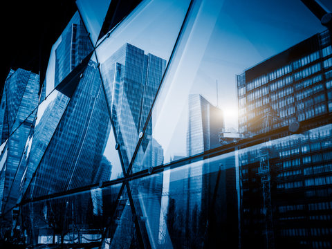 View of a modern glass skyscraper reflecting the buildings around,blue toned image.