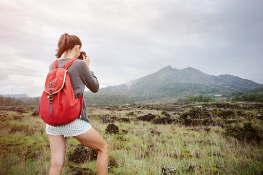 Fit traveling girl taking photo of volcano in the wild (intentional sun glare and vintage color)