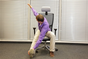 man exercising on chair in office,touching his foot, healthy lifestyle - front 