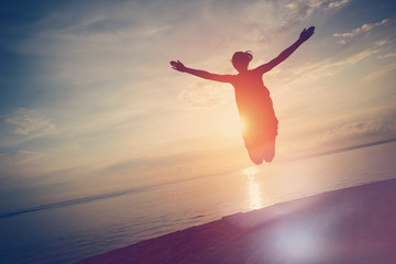 Silhouette of happy woman jumping near ocean at sunset. Intentional sun glare and lens flare effect, vintage color