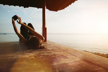 Woman touching mobile phone and resting near ocean, sun shelter on the beach. Blurry effect, lens...