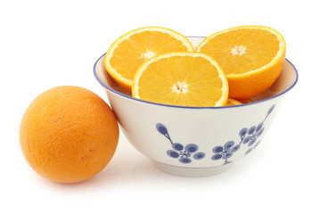 fresh oranges and some cut ones in a ceramic bowl on a white background