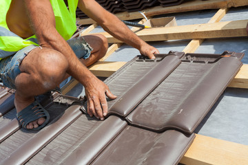 Hands of roofer laying tile on the roof. Installing natural red tile.