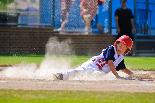 Little league baseball player sliding home.