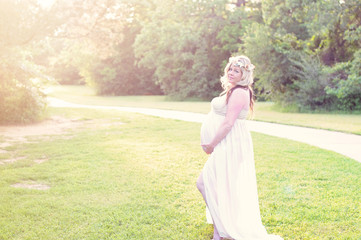 Naklejka premium Beautiful pregnant woman in a sheer dress at a park with copyspa