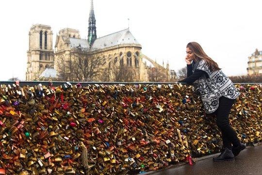 Young woman leaning against love locks, Pont de l'archeveche, Notre Dame Cathedral in background, Paris, France