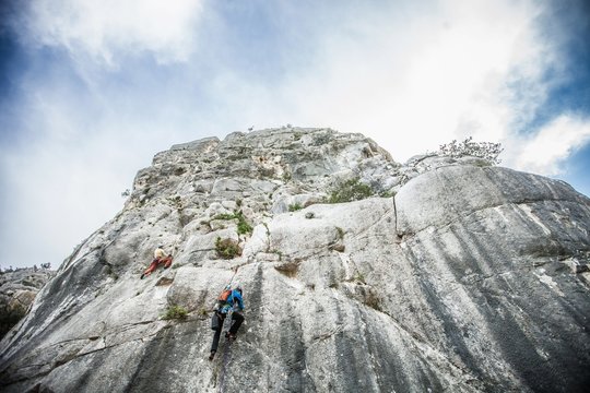 Low angle rear view of rock climber climbing up mountainside, Ogliastra, Sardinia, Italy