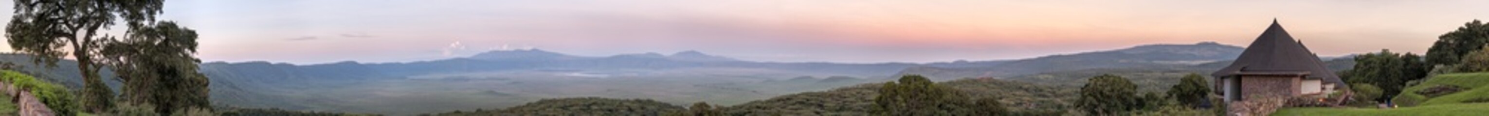 Panoramic view of huge Ngorongoro caldera (extinct volcano crater) with lodge hotel bungalows against sunrise glow background. Great Rift Valley, Tanzania, East Africa. 
