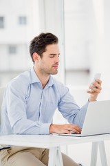 Fototapeta premium Businessman text messaging on phone while using a laptop