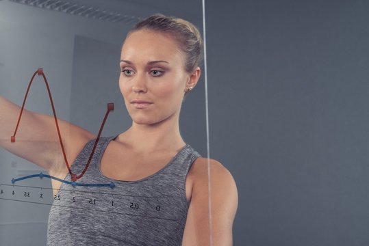 Young woman looking at chart on glass wall, grey background
