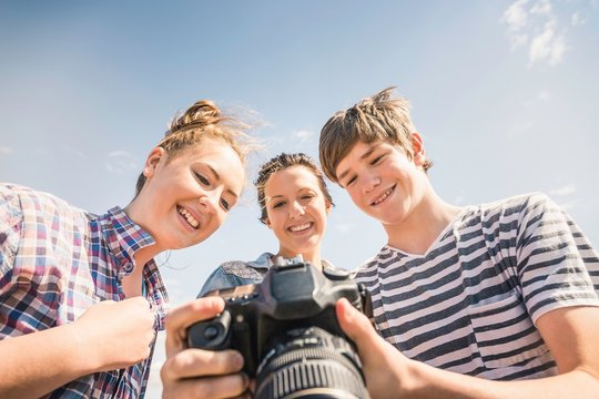 Low angle view of young man and female friends reviewing photographs on camera