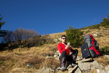 The guy in the mountains, hike with a backpack, and a solar panel for charging accumulators.