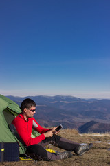 Fototapeta premium The guy in the mountains, hike with a backpack, and a solar panel for charging accumulators.