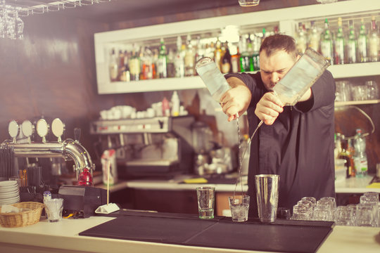 Barman hold bottle and pouring cocktail at the bar.
