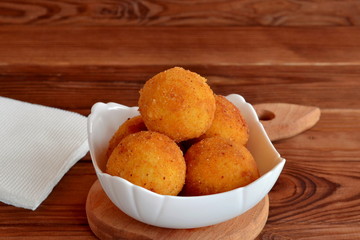 Arancini balls on a plate. Fried rice cutlets recipe. Brown wooden background 