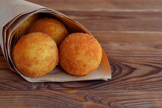 Arancini rice balls. Fried rice balls in paper on brown wooden background. Snack, street food