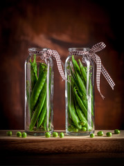 Peas in two glass jars on wooden table and dark background