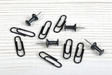 Closeup black thumbtacks and clips on light wooden surface