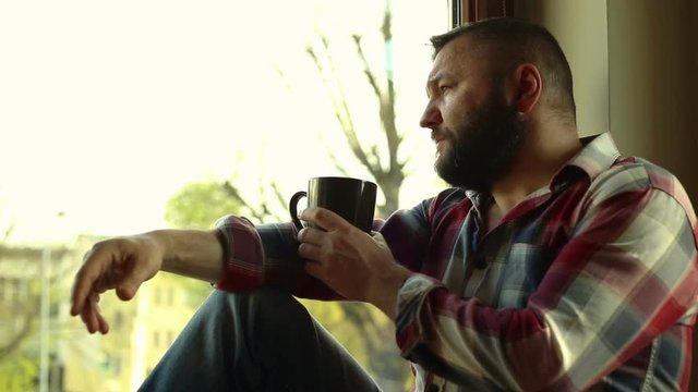 Thoughtful man drink coffee, sitting near window
