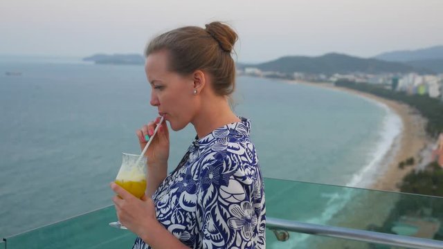 Pretty young woman drinking jouce through a straw and enjoying the view