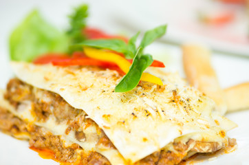 Closeup elegant serving of lasagne and small salad sitting on white plate