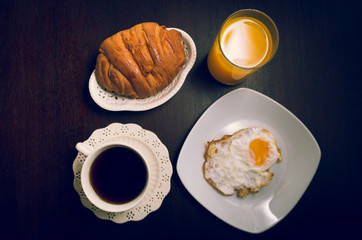 Breakfast menu shot from above including plate of cheese and butter next to coffee cup plus bread with fried egg on dark wooden surface