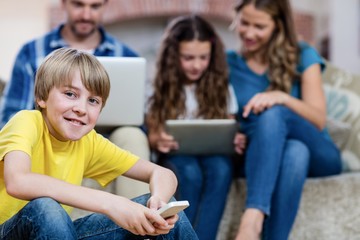 Portrait of boy using a mobile phone while family in background