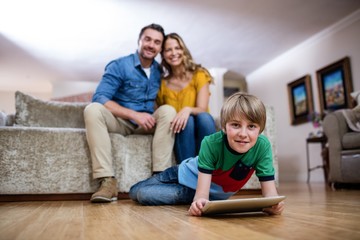 Boy using a digital tablet while parents sitting on sofa in background