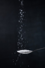 Pile of sugar in a teaspoon on a dark background. Sugar pouring from the top.