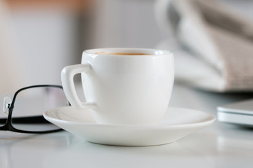 Close up view of white coffee cup on table with glasses and news