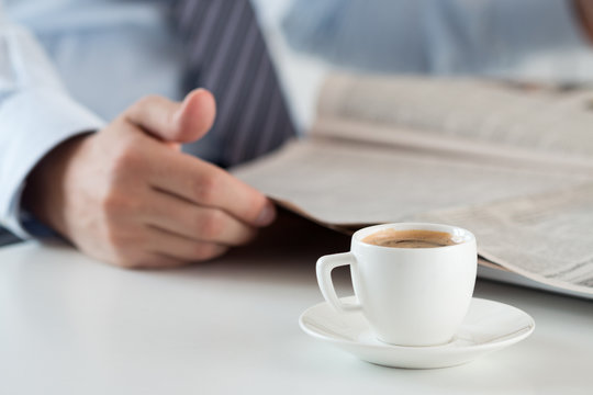 Morning espresso cup with busiessman reading newspaper on backgr