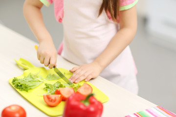 Obraz na płótnie Canvas Little girl's hands cutting vegetables on a board.
