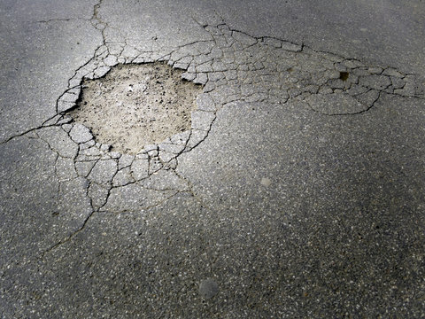 Cracked damaged asphalt street with a big hole