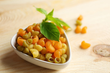 Dry multicolored gomiti pasta in white bowl on wooden table