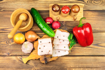 Piece and sliced fresh, raw pork lard on wooden board with vegetables, spices on the table.