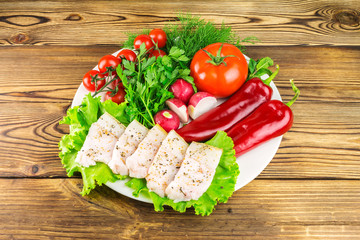 Plate with sliced fresh pork lard, fresh produce, vegetables on the wooden table.