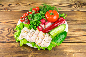 Plate with sliced fresh pork lard, fresh produce, vegetables on the wooden table.