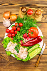 Plate with sliced fresh pork lard, fresh produce, vegetables on the wooden table.