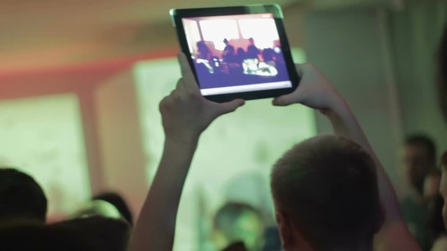 Concert in the nightclub, people dancing, man filming popular band with tablet