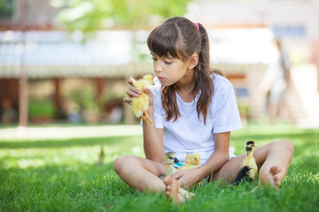 Cute girl sitting on grass and holding spring duckling 