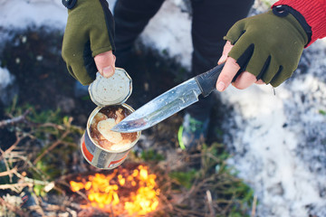 Hands holding an open jar of canned meat and a knife