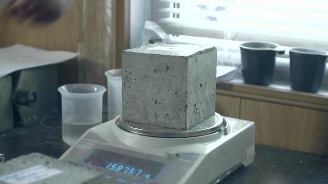 Сheckweigh of fresh grey concrete bricks in the factory or at the construction site. Male worker taking one brick out of the row. 