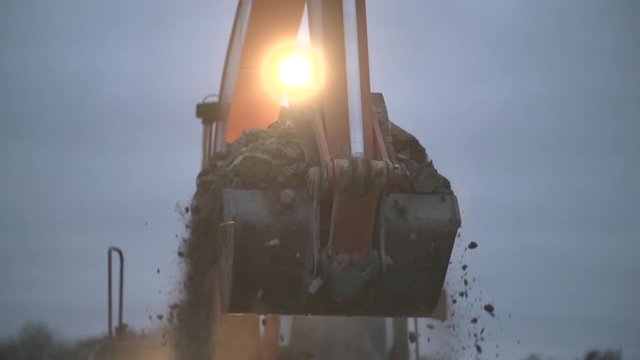 Bulldozer charging and uncharging shovel with sand and transporting to pile, close up, excavator creating heap at  construction site. Separating ground. Slow motion shot in the dusk.