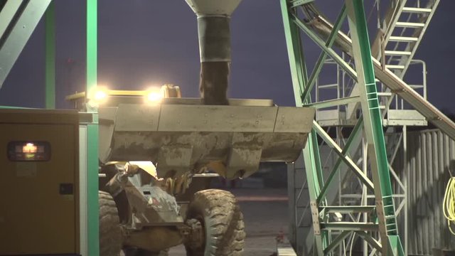 Heavy machine pouring sad or gravel into excavator shovel. Slow motion shot in the night. Excavator in use in the dark. 