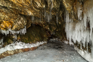 Multicolored stone cave in the cliff with icicles.