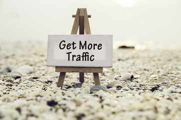 conceptual image with word GET MORE TRAFFIC on white canvas frame with wooden tripod stand.Blurred Clamshell and cockles background.