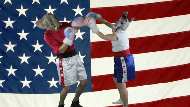 Man in elephant GOP mask and woman in donkey Democrat mask wearing boxing shorts throwing childish punches againstagainst an American Flag.