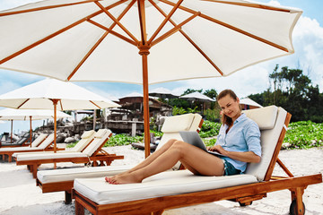 Summer Work. Portrait Of Smiling Business Woman Relaxing On Sun Lounger And Using Laptop Computer Outdoors. Beautiful Happy Girl Working Online At Beach By Sea. Communication Technology Concept.